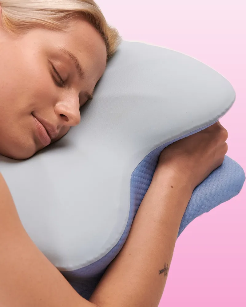 Woman asleep on her side hugging a light-blue butterfly-shaped memory foam pillow